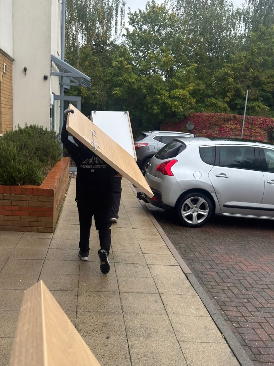 Two crew members carrying a large panel outside, with Together Logistics UK visible on a shirt